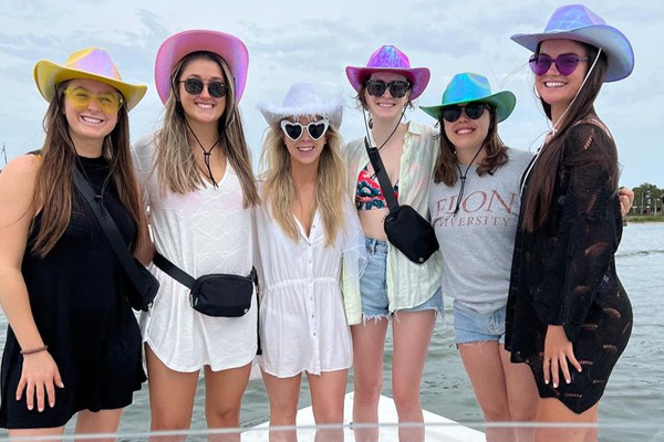 six women wearing hats and sunglasses posing on a boat